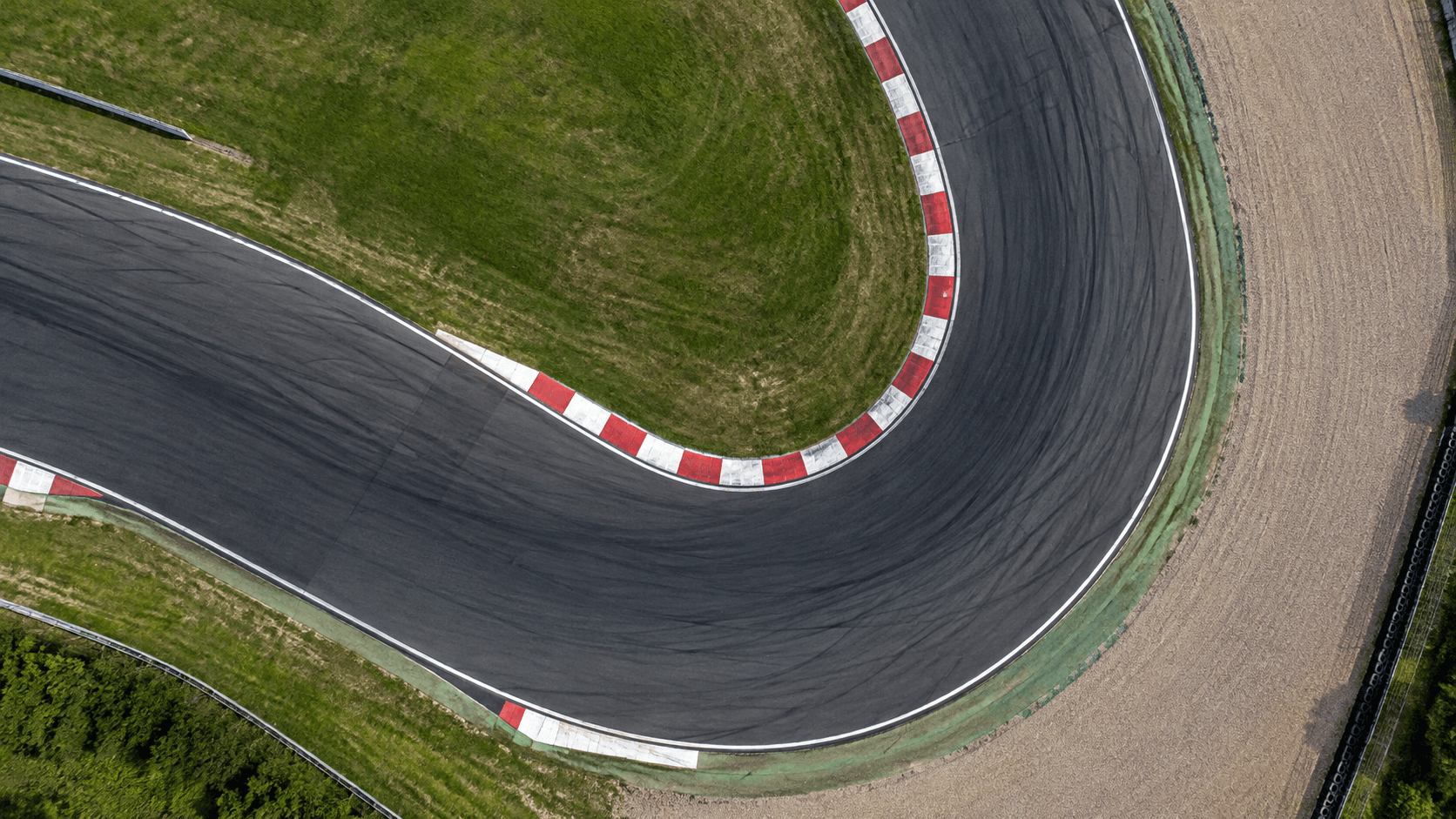 Vista aérea de uma curva de autódromo com zebras vermelhas e brancas